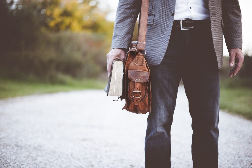 Man walking with satchel over shoulder and book in hand